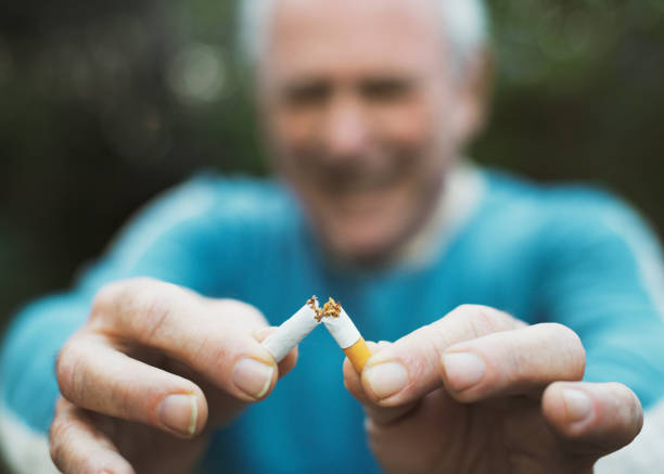 senior man quitting smoking breaks his last cigarette with a smile - breaking cigarette imagens e fotografias de stock