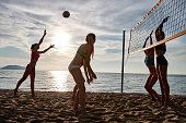 Young woman in bikini playing beach volley with friends, serving the ball