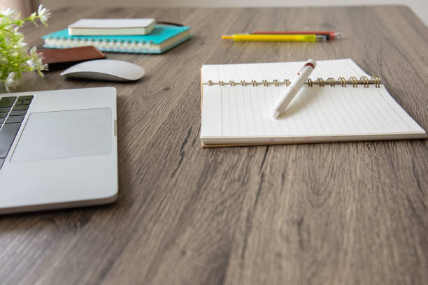 istock A side view with selective focus of a business desk includes opening book, a multi-colored pens, books, computer laptop, mouse and flowers on a wooden table to connect with others in the digital technology world with copy space. 1267171913