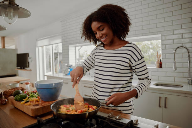 woman mixing ingredients and vegetables in pan while preparing lunch - cozinhar imagens e fotografias de stock