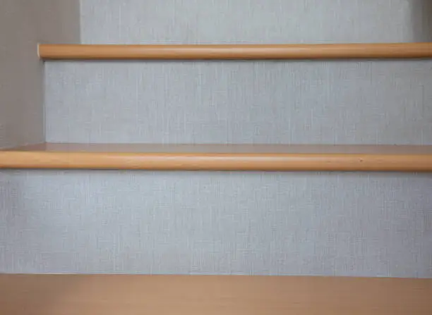 Photo of The front and close-up view of the wooden stairs lined with gray fabric with its texture can be beautifully seen, and see the steps upstairs as a blurry background, giving the feeling and concept of living that has to walk up to success.
