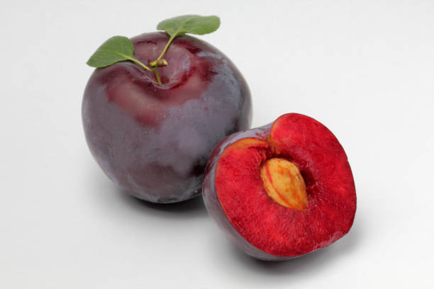 istock Large plum with natural leaves and cut fruit with bone on a white background, bright colors, high contrast. 1267178479