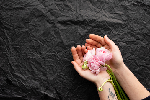 Pink tender peony in the hands of a girl. Black rumpled background. Beautiful layout of flowers. Florist collects a bouquet.