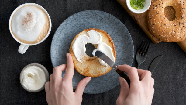 brotkäse auf bagel verteilen - streichkäse stock-fotos und bilder