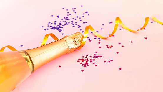 Champagne bottle with confetti on pink  background. Blurred effect. Creative space for Christmas design. Close-up