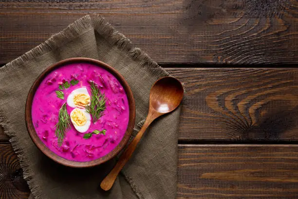 Delicious, healthy cold beetroot soup, decorated with egg and dill on a wooden table. Top view. Healthy eating. Diet food concept.