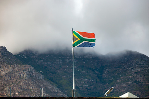 View of the national flag of the Republic of South Africa on the background of Table mountain in Cape town. South Africa flag in the wind against the background of fog and clouds and mountains in Cape town.  Africa,