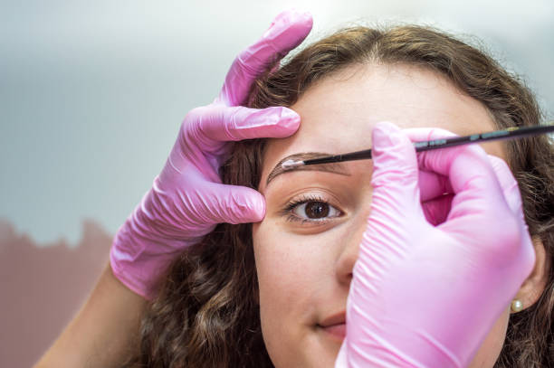 eyebrow master makes an eyebrow correction to a young woman. Henna eyebrow coloring procedure in a beauty salon stock photo