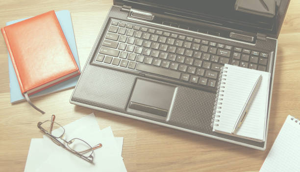 istock Workplace with laptop, notebook and glasses on a wooden table. Telework. Work from home. Blurred background 1267184020