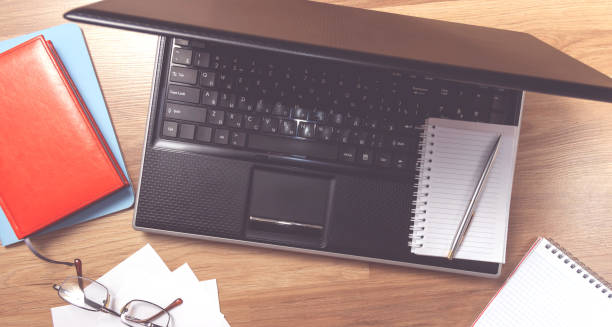istock Workplace with laptop, notebook and glasses on a wooden table. Telework. Work from home. Blurred background 1267184027