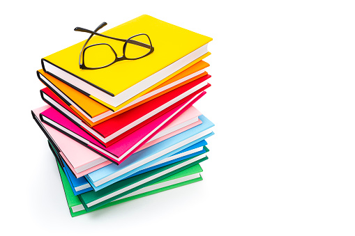 High angle view of rainbow colored books arranged in a stack isolated on white background. Eyeglasses are on the book stack. Useful copy space available for text and/or logo. High resolution 62Mp studio digital capture taken with SONY A7rII and Zeiss Batis 25mm F2.0 lens