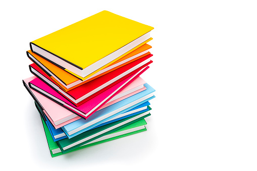 High angle view of rainbow colored books arranged in a stack isolated on white background. The composition is at the left of an horizontal frame leaving useful copy space for text and/or logo at the right.High resolution 42Mp studio digital capture taken with SONY A7rII and Zeiss Batis 40mm F2.0 CF lens
