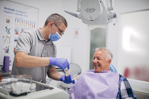 Male dentist explaining denture work to senior patient in dental clinic.