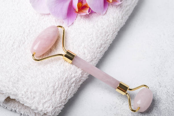 istock Rose Quartz jade roller and Gua Sha massager on towel on stone background. Close-up. Massage tool for facial skin care, SPA beauty treatment concept 1267190570
