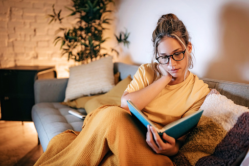 Young women reading book at home in sofa