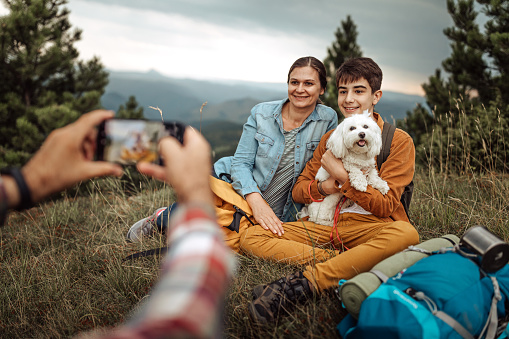 Man photographing wife and son with pet dog on hiking tour using mobile phone camera at forest