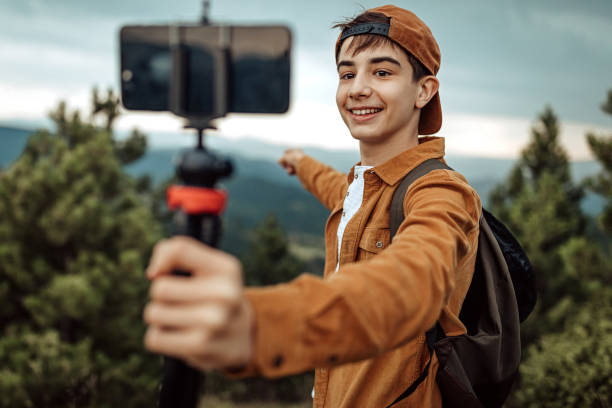 Boy hiking and vlogging using mobile phone Teenage boy using mobile phone handheld gimbal for travel vlogging social media kids stock pictures, royalty-free photos & images