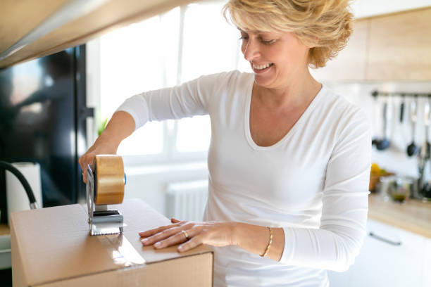 istock Woman enjoying packing cardboard box, using adhesive tape dispenser 1267193246