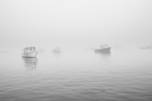 A group of lobster boats sit ready to work on a grey and foggy day