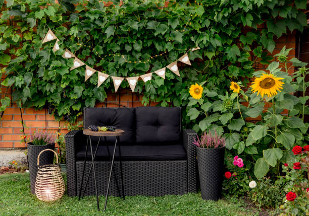 schwarze moderne polyrotang gartenmöbel stuhl, metalldraht beistelltisch. grüne weinreben pflanzen wachsen auf roten ziegelwand als dekoratives element. bambus-kerze laterne beleuchtet, rosa heideblume. - fruit table bamboo black stock-fotos und bilder