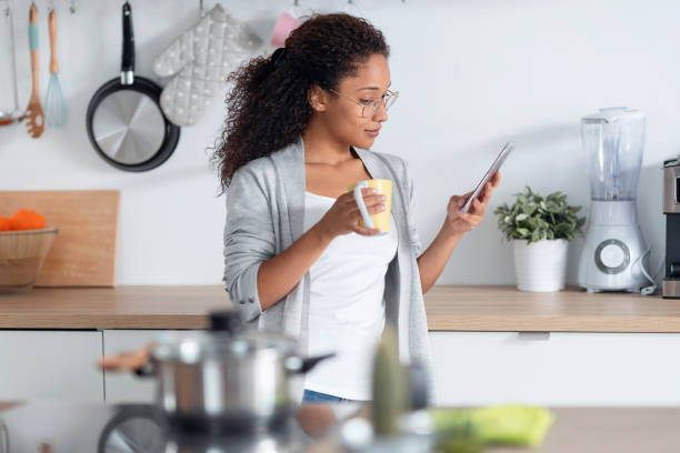 istock Beautiful young woman using her mobile phone while drinking a cup of coffee in the kitchen at home. 1267198767