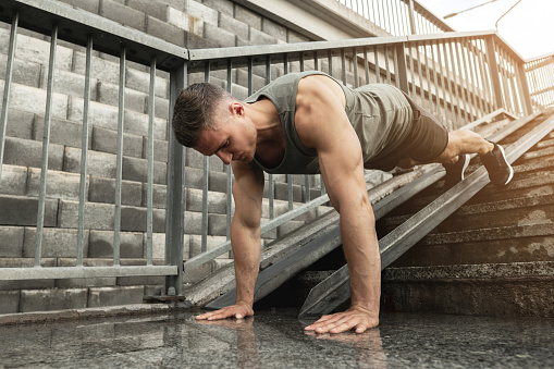 Young and muscular man is doing push-ups during calisthenic workout on a street