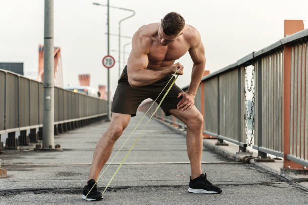 homem musculoso durante o treino com uma resistência elásticos em uma árvore - muscular build men human muscle body building exercises - fotografias e filmes do acervo