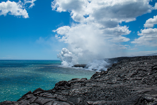 Volcanic Landscape Lava flowing in the ocean on big island Hawaii and creating clouds of steam. The picture was taken from the coast standing on cooled down lava stone.