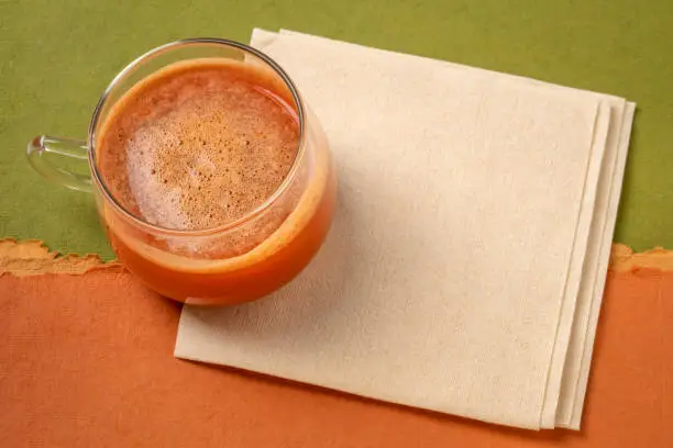 a glass cup of fresh home made carrot juice on a napkin against colorful paper abstract, healthy eating concept