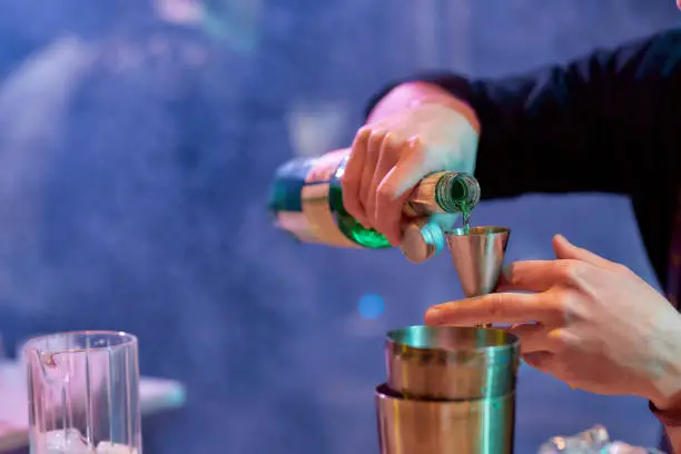 Photo of Close up of hands of male bartender pouring, mixing ingredients while making cocktail alcoholic drink at the bar counter in the night club