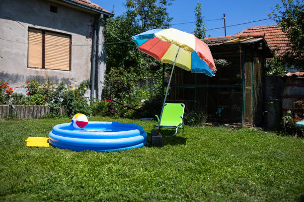 An inflatable swimming pool with a beach ball floating in it and a beach chair next to a sunshade are in a back yard