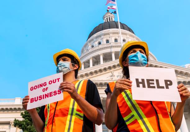 Construction workers demonstrating outside a government building wearing protective face mask holding help and going out of business signs