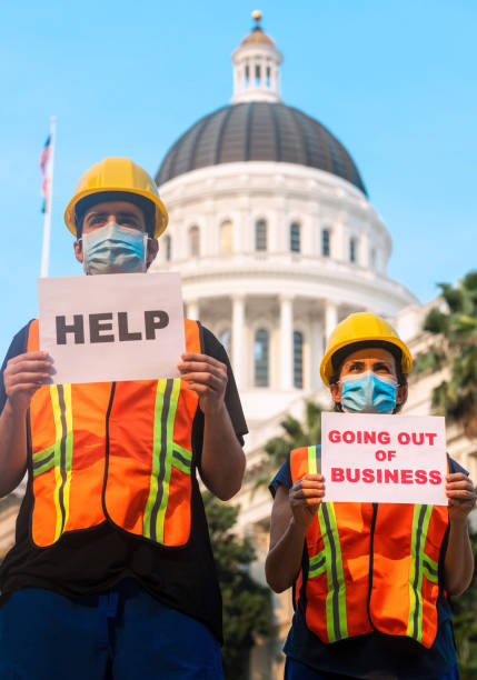 istock Construction workers demonstrating outside a government building wearing protective face mask holding help and going out of business signs 1267216928
