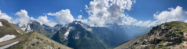istock Panorama. Snowy mountain against cloudy sky. From below white clouds floating on blue sky over mountain ridge covered with snow on sunny day in nature 1267216970