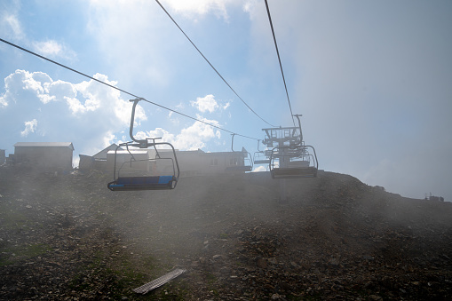 Clouds enveloping modern ropeway with benches in amazing mountainous terrain.