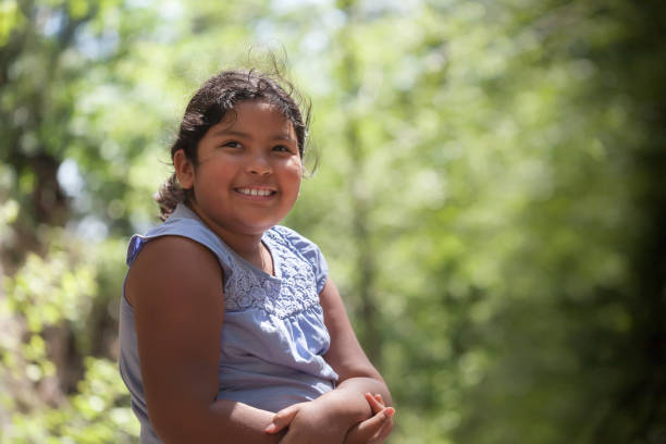 A young latino girl with a smile who is enjoying natures beauty, surrounded by trees with green foliage. stock photo