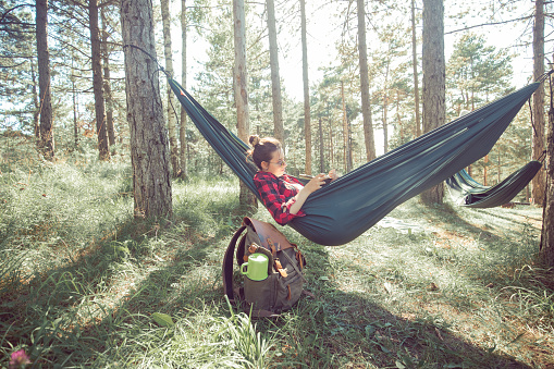 A young woman is sitting in a hammock she'd set close to the remote hut she owns. She's enjoying her day off work and noisy life.