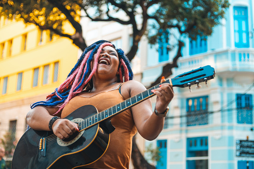 Woman with rastafarian hair style playing acoustic guitar on the street