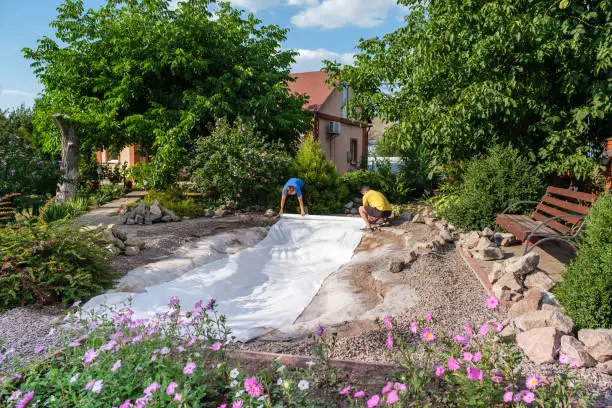 Photo of Family roll out a roll of white non-woven geotextile fabric to set up fish pond