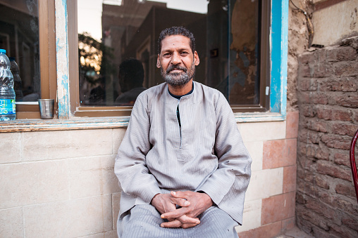 Luxor / Egypt - December 15, 2019: portrait of egyptian man with traditional clothes and pretty eyes sitting on street