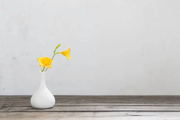 yellow day-lily flowers in white vase on wooden table