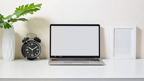 istock Mock up of creative workspace with laptop, frame pictures, clock and vase on white table and white background. Front view. 1267250146