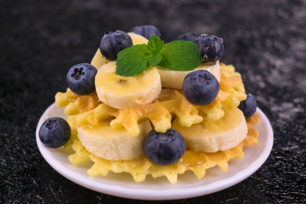 Delicious waffles with banana and blueberries on a black background. Close-up.