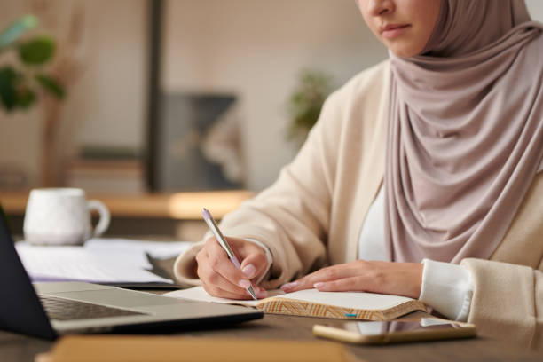 istock Unrecognizable Middle Eastern woman wearing headscarf working at office table writing something in her notebook 1267254253