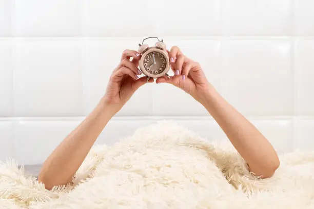 Photo of Alarm clock in female hands in a white bed, the concept of time, a wonderful start to a new day, good morning