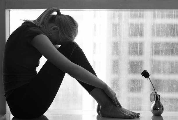 istock Sad woman sitting alone by the window next to a rose. Relationship difficulties and breakup. 1267268329