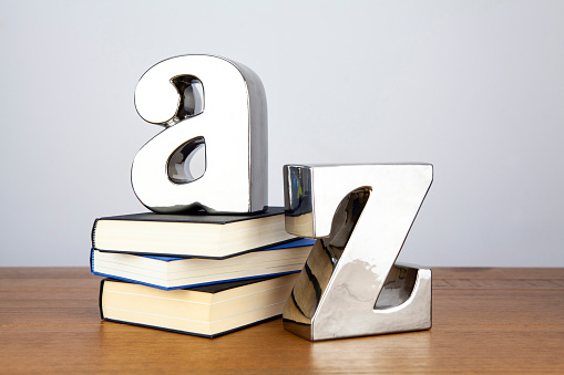 Stack of books on a wooden surface with silver coloured A and Z bookends standing on the top and by the side of the books