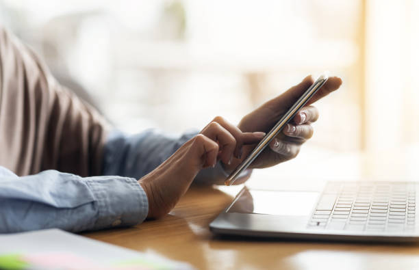 istock Female hands holding smartphone and using laptop 1267273028