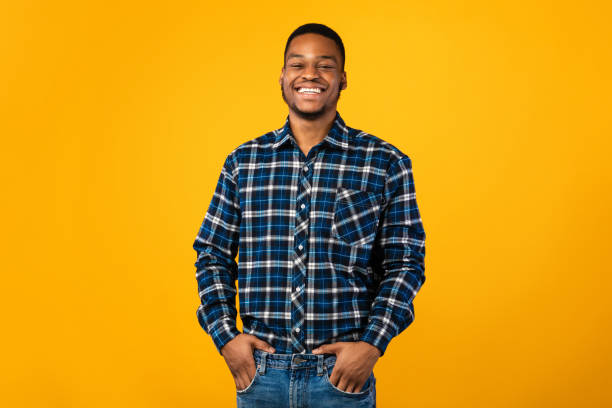 istock Black Guy Smiling Standing Holding Hands In Pockets, Yellow Background 1267273118