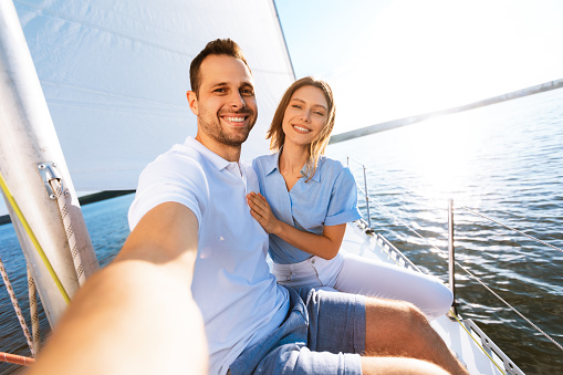Yacht Cruise. Couple Making Selfie Sitting On Sailboat Deck Enjoying Sailing On Vacation At Seaside. Selective Focus